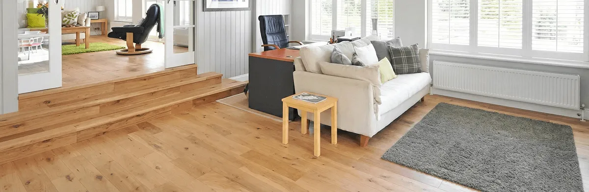 A modern living room with professionally installed laminate flooring, a beige sofa, a small side table, a gray rug, and large windows with white shutters in Omaha, NE